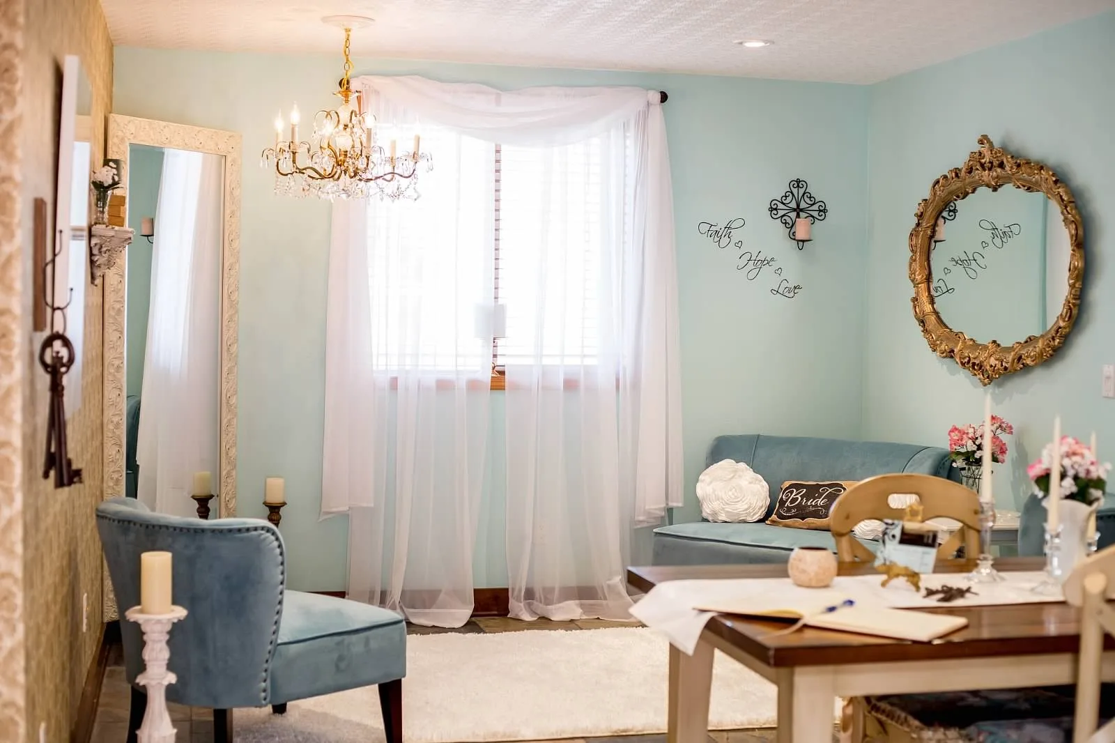 Elegant bridal suite with teal velvet furniture, crystal chandelier, ornate gold mirror, and Faith Hope Love wall decor at Mountain View Manor wedding venue in Enumclaw Washington near Seattle