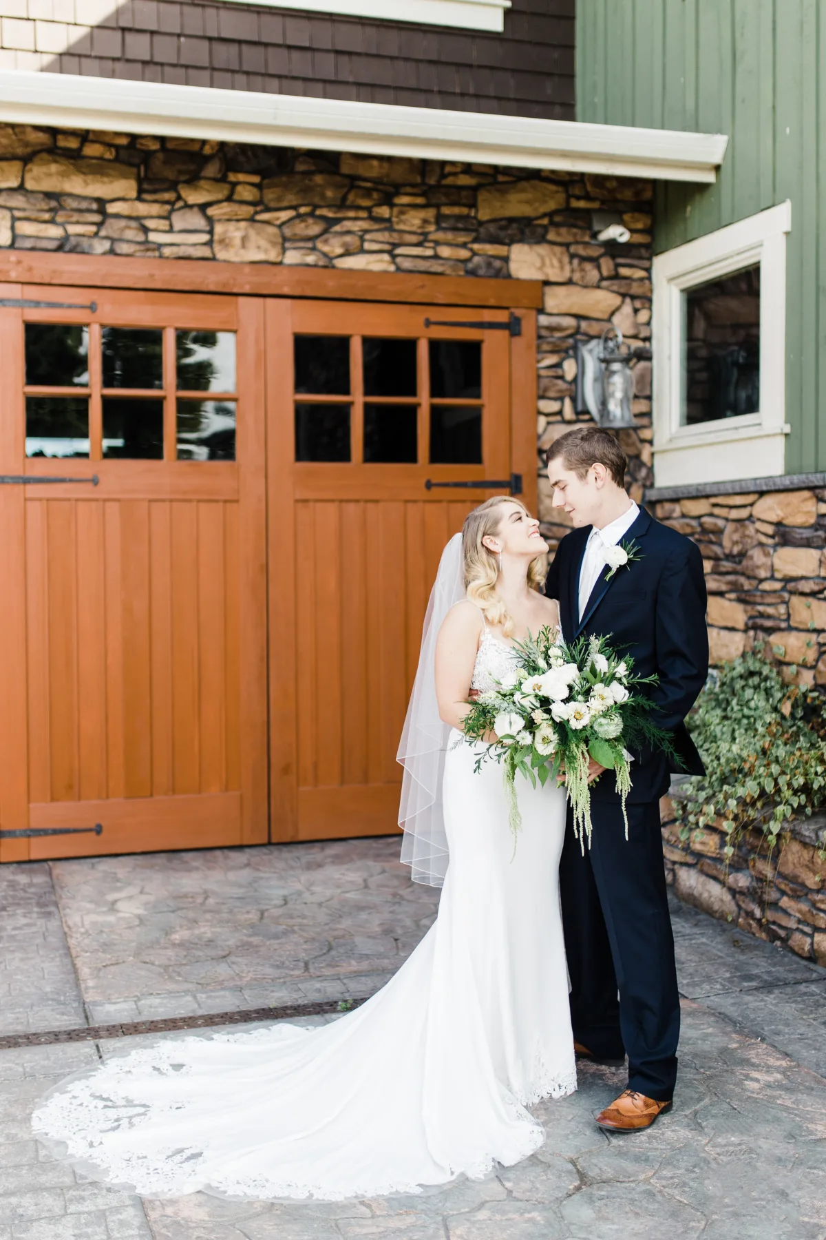 bride groom portrait mountain view manor enumclaw washington - Packages & Pricing Bride in a lace-trimmed gown with veil holding a lush white and green bouquet gazes up at her groom in a navy suit outside Mountain View Manor wedding venue in Enumclaw Washington near Seattle