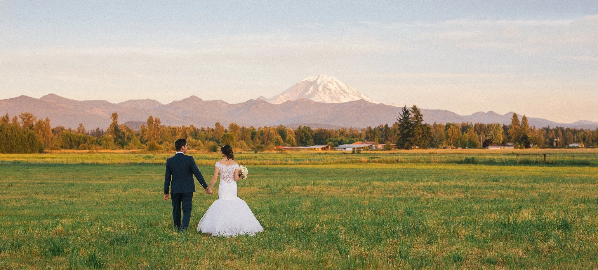 bride groom walking mount rainier enumclaw washington - Mountain View Manor Bride and groom holding hands walking through a green field with Mount Rainier in the background at Mountain View Manor wedding venue in Enumclaw Washington near Seattle