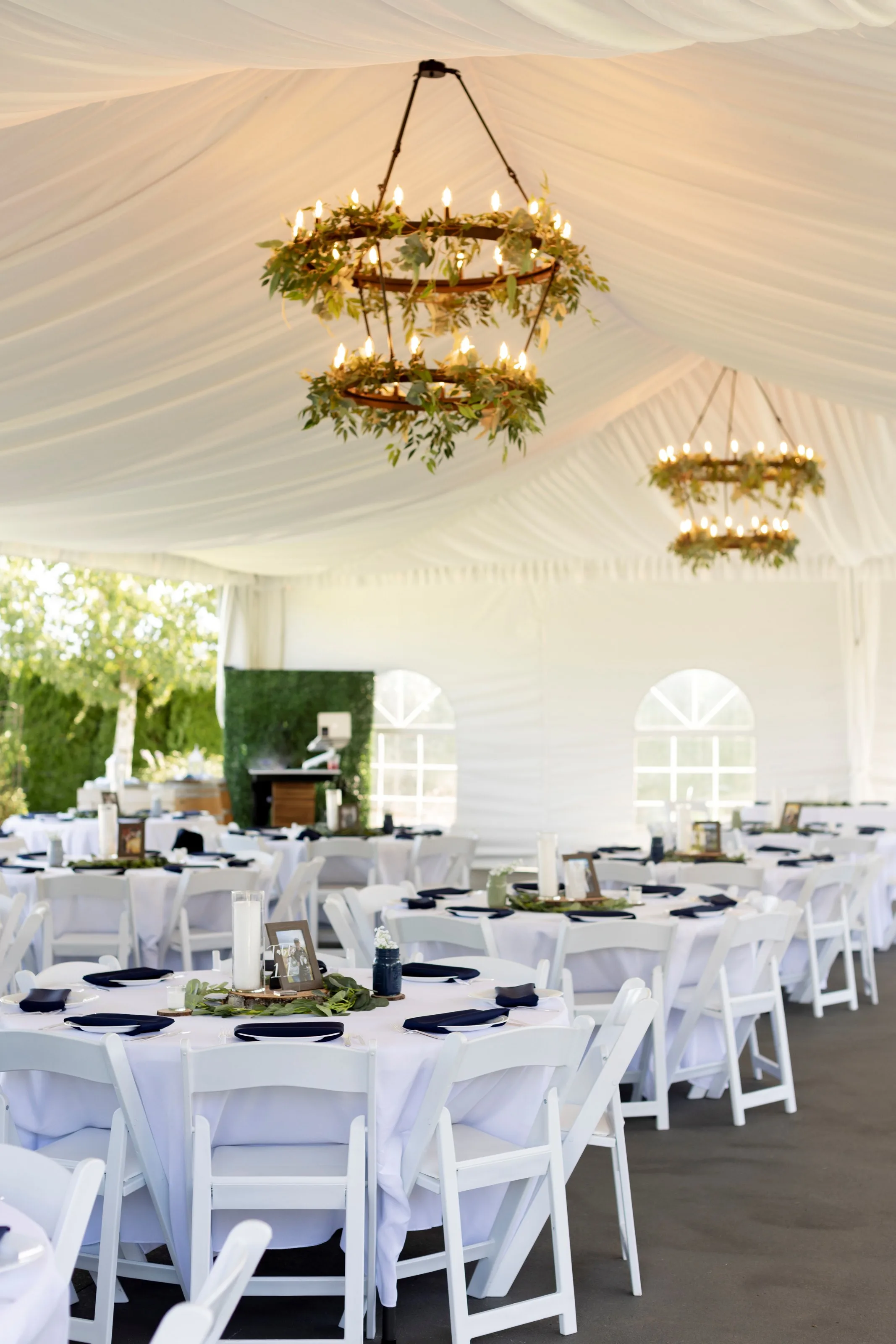 wedding reception tent chandeliers mountain view manor enumclaw - Private Events Elegant tented wedding reception at Mountain View Manor in Enumclaw Washington featuring tiered greenery chandeliers white folding chairs and navy blue place settings on round tables